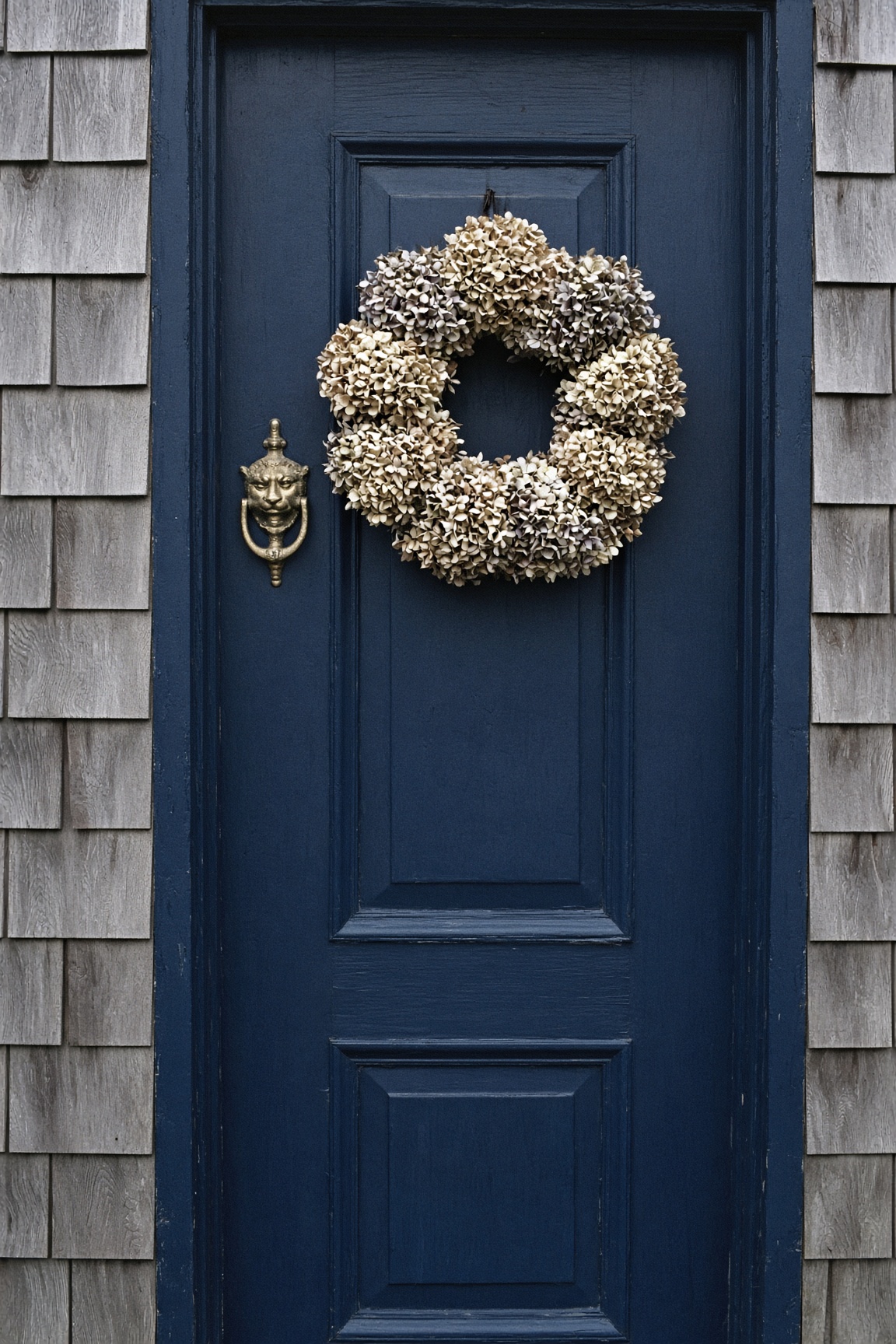 Navy front door with a dried hydrangea wreath on a cedar-shingled house