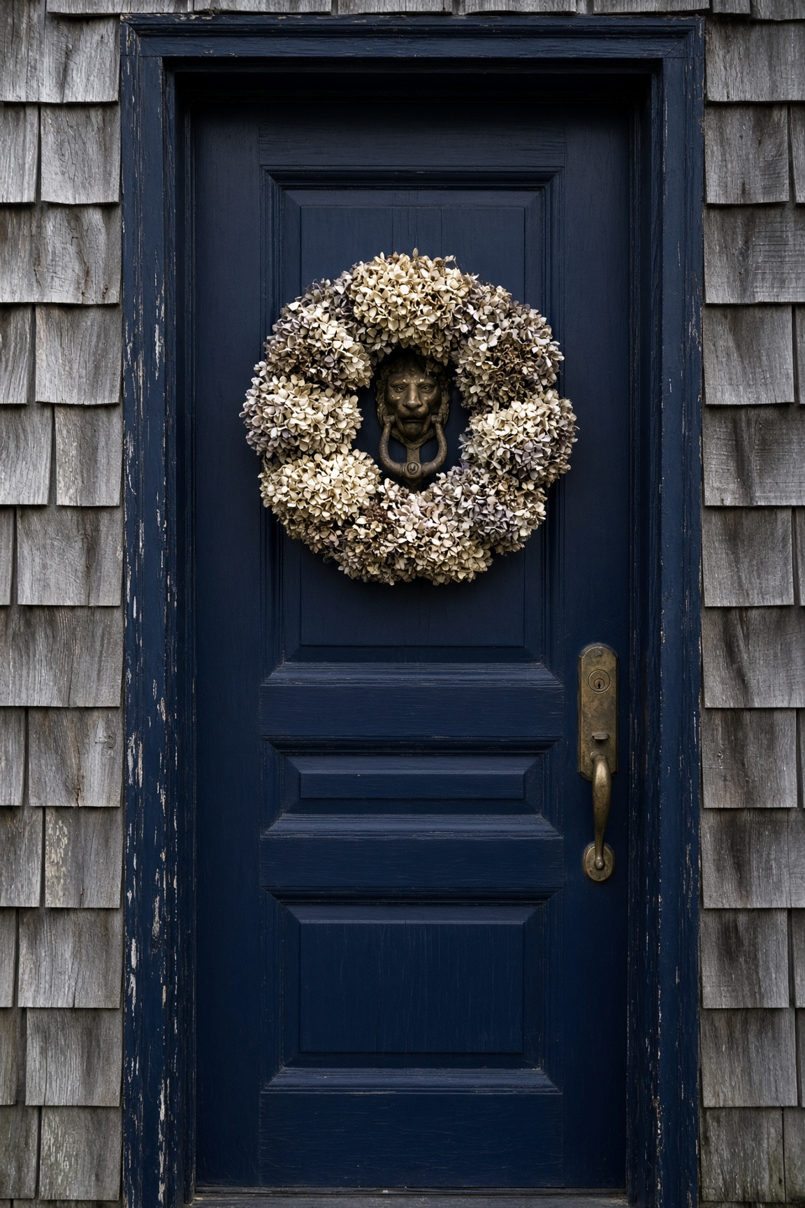 Navy front door with a dried hydrangea wreath set in weathered cedar shingles